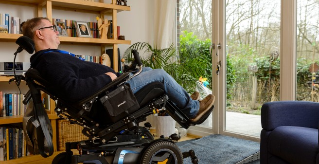 Tomas Gerlach in seinem Wohnzimmer. Er entspannt, halb liegend, im Rollstuhl und schaut in den Garten
