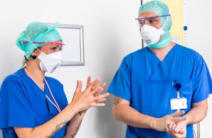 Dana Möller und Steffen Lamprecht mit Atem-, Gesichtsschutzmasken und grünen Tüchern über den Haaren desinfizieren ihre Hände