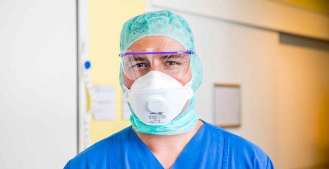 Steffen Lamprecht mit Atemschutzmaske und Gesichtsschutzhelm blickt in die Kamera