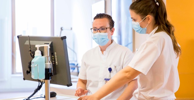 Dr. Louise Roggelin und ein Kollegin stehen nebeneinander ung Blicken auf einen Monitor. Beide tragen weiße Arbeitskleidung und einen Mund-Nasen-Schutz