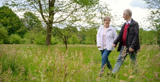 Peter Seifert und seine Frau gehen durch eine Wiese. Sie lächeln sich an, Peter Seifert schreitet kräftig aus.