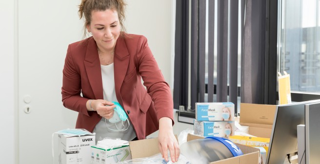 Vor Janna-Lynn Schröder liegen auf einem Schreibtisch sehr viele unterschiedliche Masken in verschiedenen Verpackungseinheiten. Sie greift nach einer davon