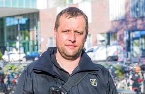 Ricardo Zbirski seht auf einem Seitenweg vor dem Haupteingang des UKE, im Hintergrund rechts mehrere Fahrräder. Er blickt in die Kamera