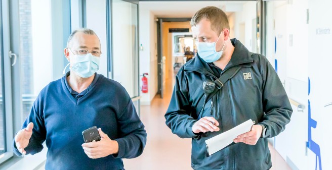 Waldemar Ringe und Ricardo Zbierski gehen nebeneinander durch einen Klinikgang, sie tragen Mund-/Nasenschutz Masken