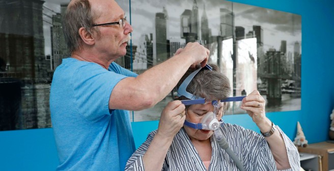 Rainer Kollrich verschnürt die Atemmaske am Hinterkopf seiner Frau Karin