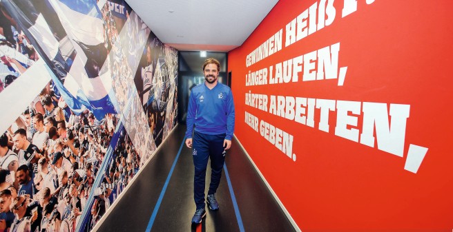 Daniel Petrowski geht durch einen schmalen Gang auf den Fotografen zu. An der Wand Bilder jubelnder Fans und folgender Text: Gewinnen heißt: Länger laufen, Härter arbeiten, Mehr geben.