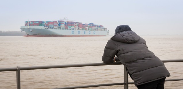 Jugendlicher an der Elbe blickt auf Containerschiff