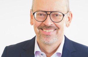 Prof Aepfelbacher geht auf der Treppe auf den Fotografen zu. Er trägt Jeans und Jacket, eine Hand lässig in der Tasche