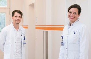 Prof. Weisel und Dr. Böschel stehen coronabedingt weit auseinander im Flur der Klink. Sie lächeln in die Kamera