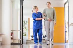 Eine Patientin wird von einer Pflegerin beim Gehen im Flur begleitet