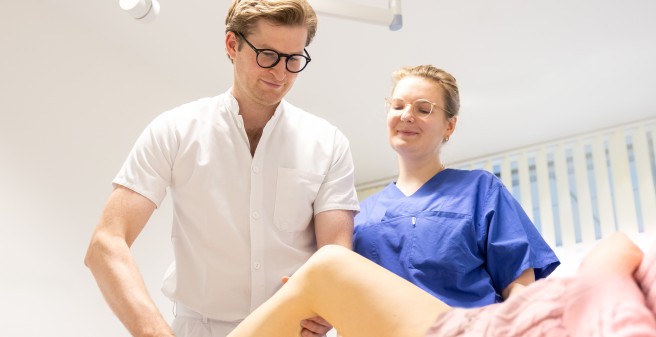 Ein Orthopädie und eine Ärztin in Weiterbildung untersuchen eine Patientin nach ihrer OP