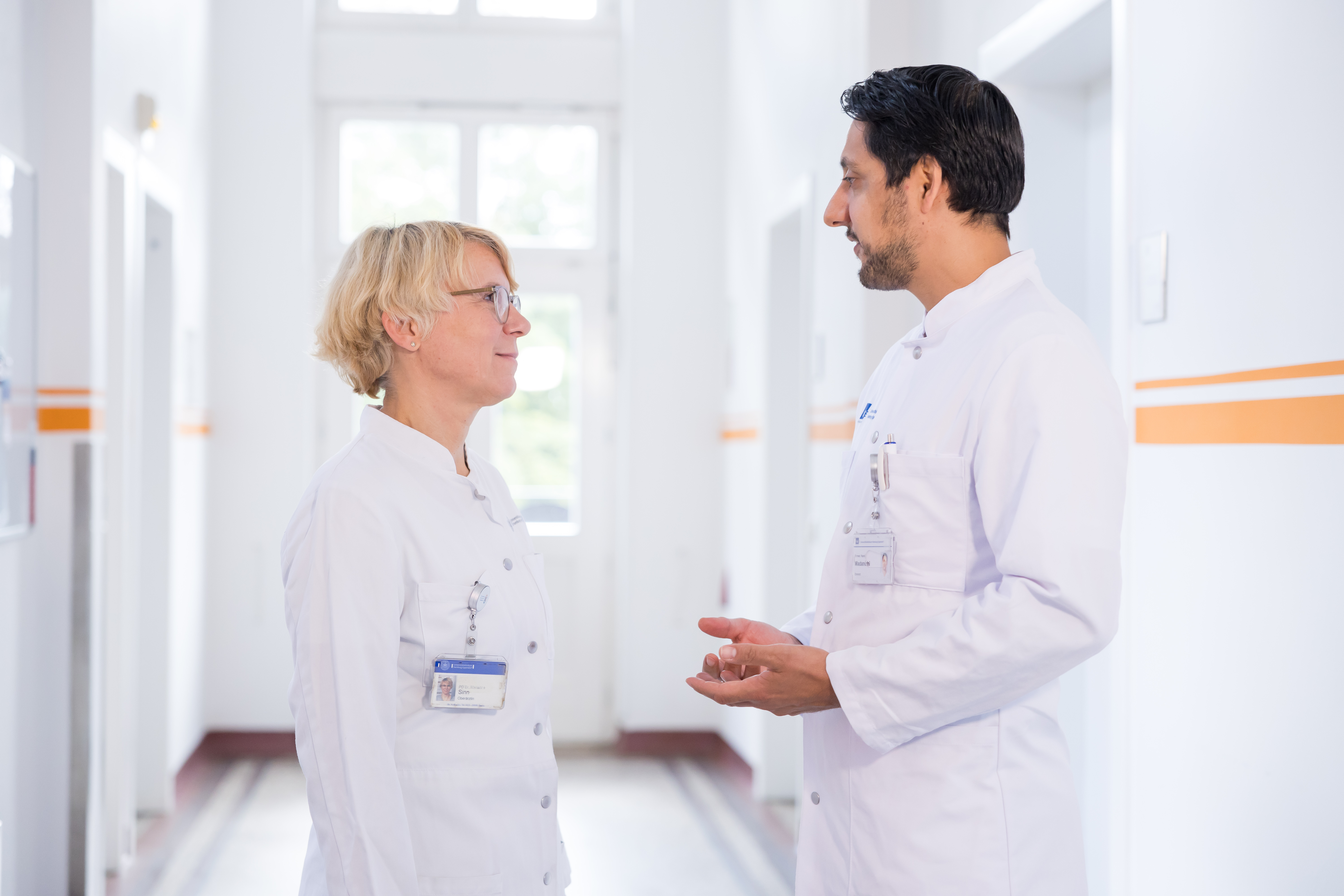 A male doctor and a female doctor are talking to each other in a hallway.