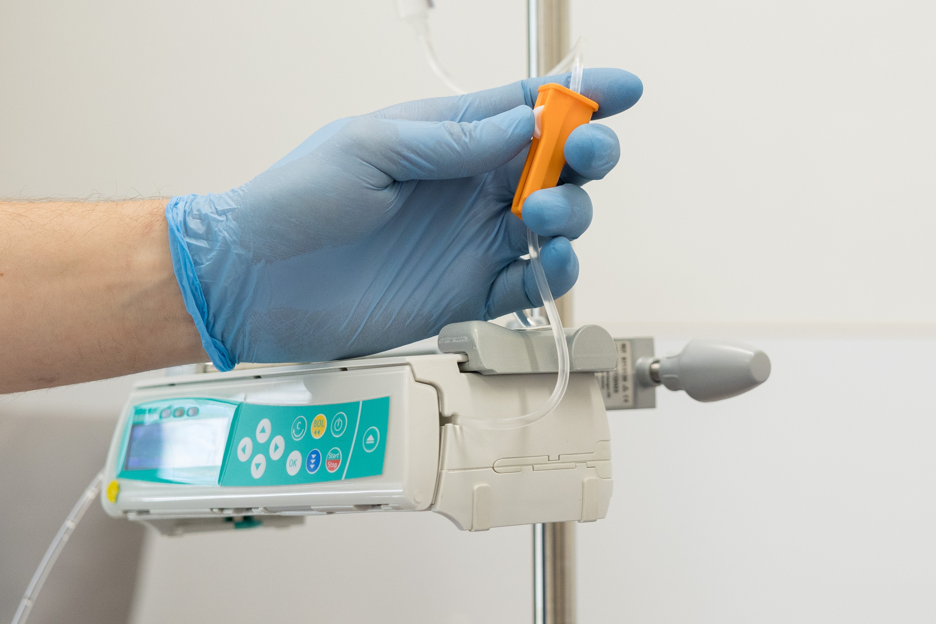 Hand mit Gummihandschuh stellt die Durchflussgeschwindigkeit an einem Infusionsständer ein.