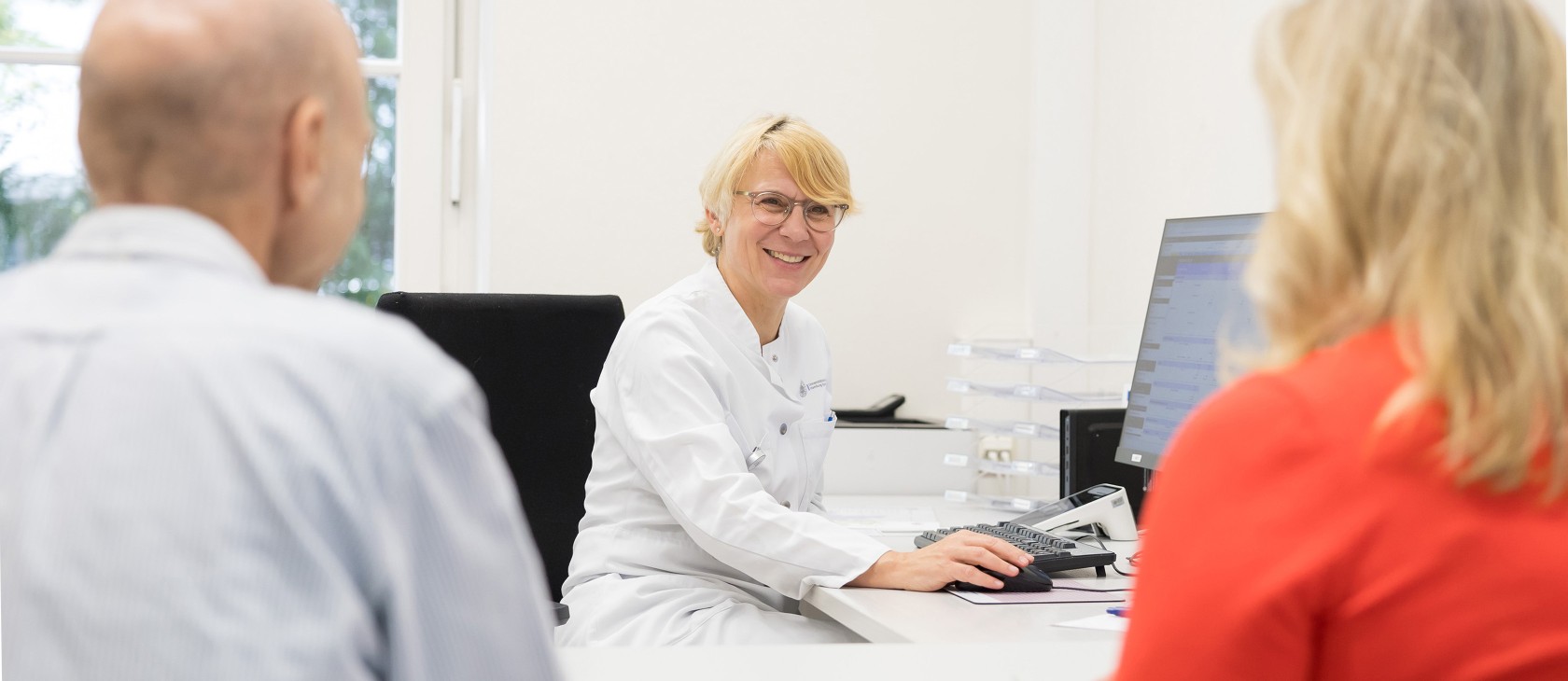 Onkologin während einer Sprechstunde am UCC Hamburg mit Patient und Angehörige lächelt in die Kamera. 