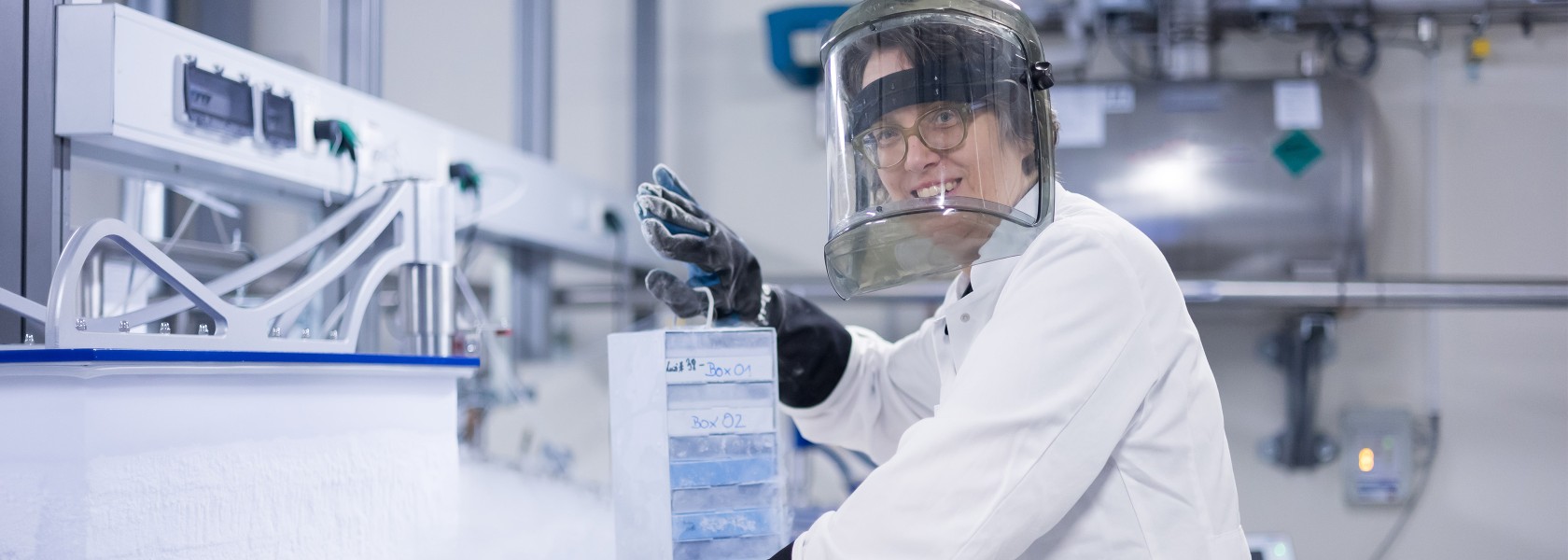 Scientist in nitrogen tank laboratory looks into the camera while pulling a sample container out of a tank.