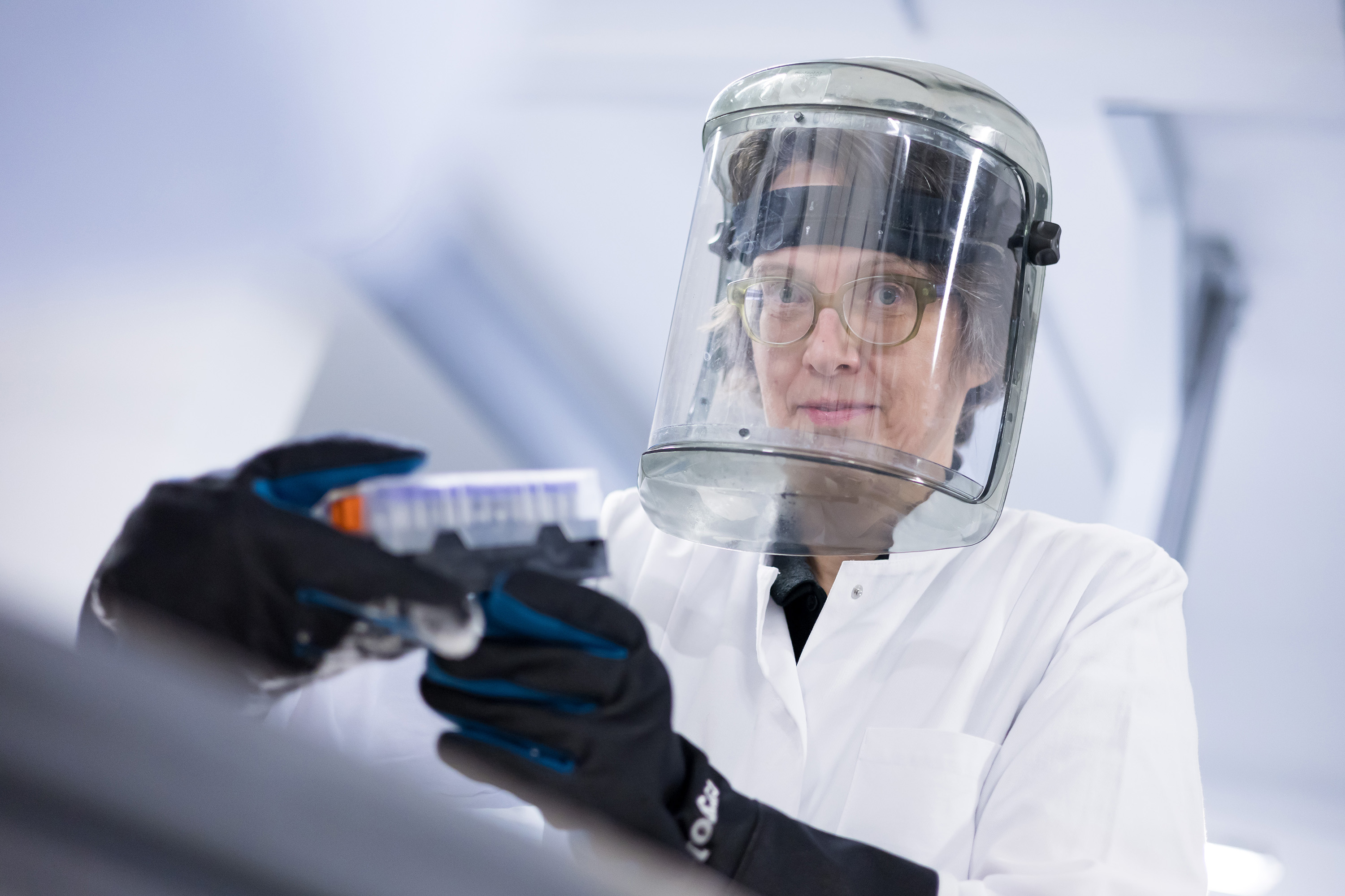Eine Person hält einen Probenbehälter in der Hand und schaut in die Kamera