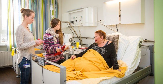 Auszubildende zur Diätassitentin in Besprechung mit Patientin, die im Bett liegt